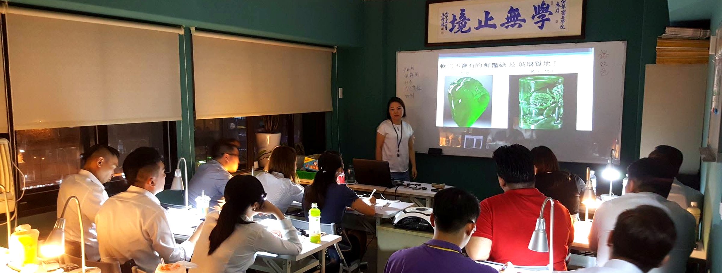 伊犁寶石鑑定所教室現場：講師於投影幕前授課，牆上懸掛「學無止境」匾額